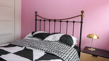 Una cama con colcha a cuadros blanco y negro, un cabecero de metal y una mesita de noche con una lámpara.
