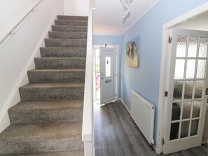 Una escalera con peldaños alfombrados que conduce a una puerta, un pasillo con radiador y un cuadro en la pared.