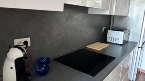 Une cuisine moderne dotée d’une plaque de cuisson à induction noire, de meubles blancs et d’une machine à café.