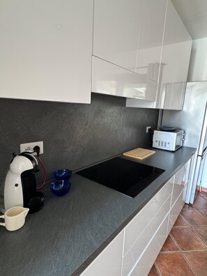 Eine moderne Küche mit einer schwarzen Induktionskochplatte, weißen Schränken und einer Kaffeemaschine.