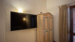 Une pièce avec un téléviseur fixé au mur, un meuble en bois et une fenêtre avec des rideaux.