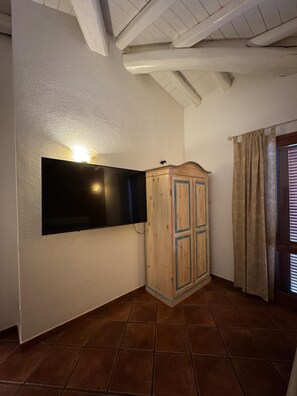 Ein Zimmer mit an der Wand befestigtem Fernseher, einem Holzschrank und einem Fenster mit Vorhängen.