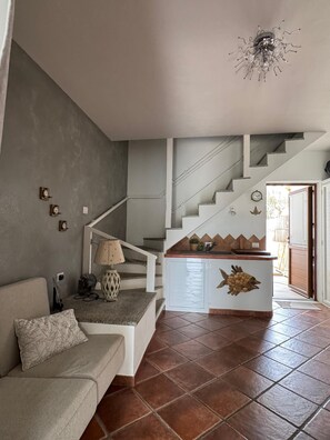 A living room with a sofa, a lamp, a staircase, and a kitchen area with a fish decoration. - Casa Su Entu Blu & Piscina (Case Peschiera-lu Fraili)