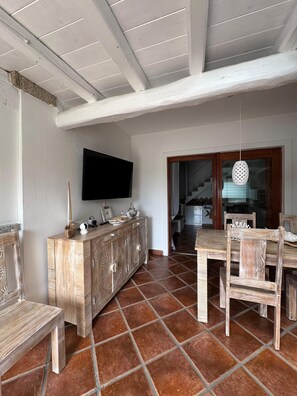 Ein Essbereich mit Holztisch und Stühlen, einem an der Wand montierten Fernseher und einem Fliesenboden.