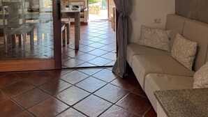 Un salon avec un canapé, une porte vitrée donnant sur un coin repas et un mur en pierre.