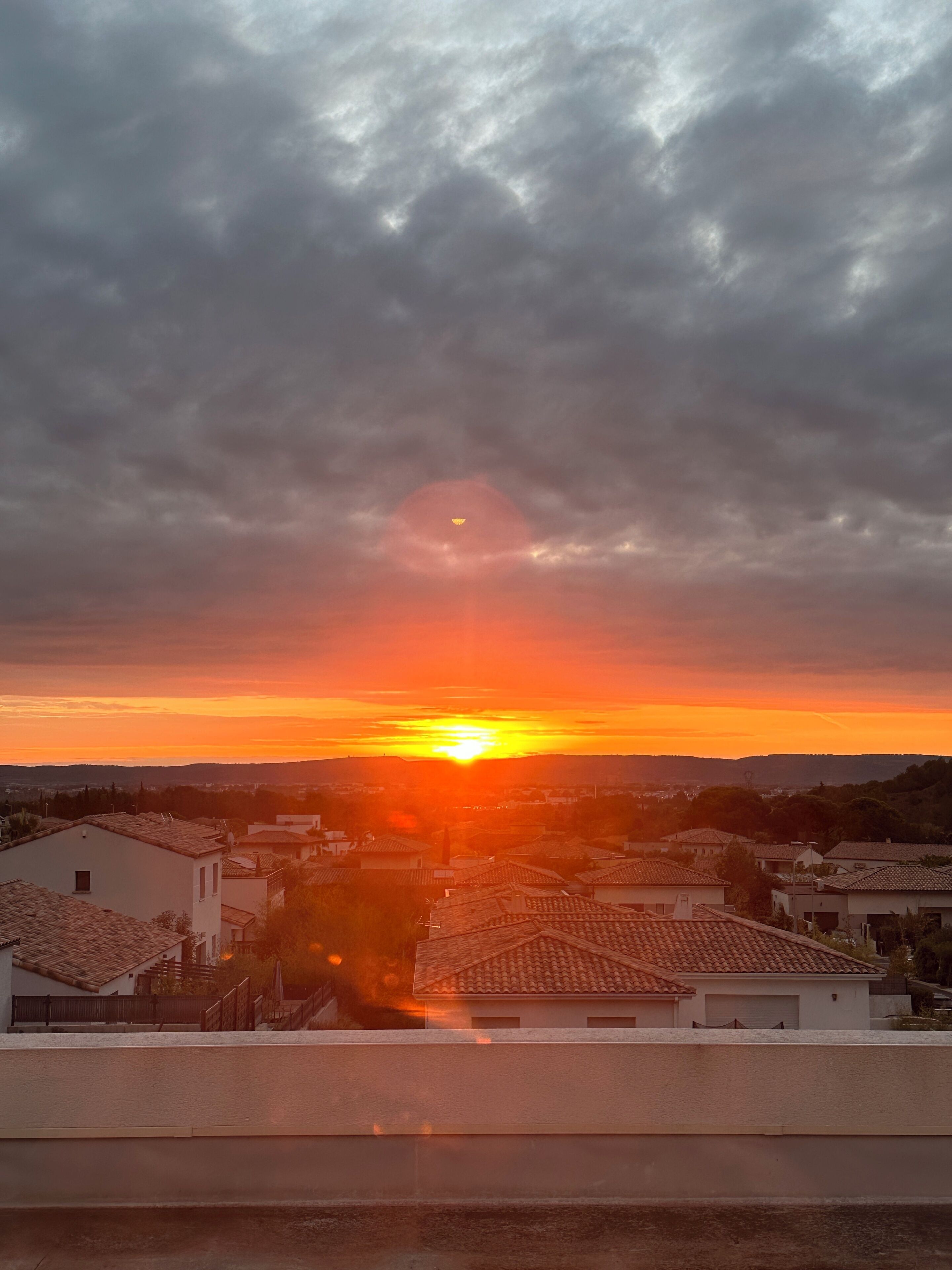 Un coucher de soleil sur une zone résidentielle, avec des maisons et un ciel dégagé.