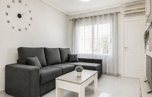 Ein Wohnzimmer mit grauem Sofa, weißem Couchtisch und einer Wanduhr.