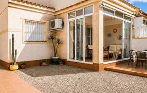 Un patio couvert aménagé avec des sièges, un pot de fleurs et un appareil de climatisation.