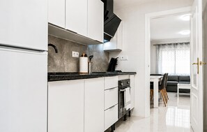 Une cuisine moderne avec des meubles blancs, un plan de travail noir et un four encastré.
