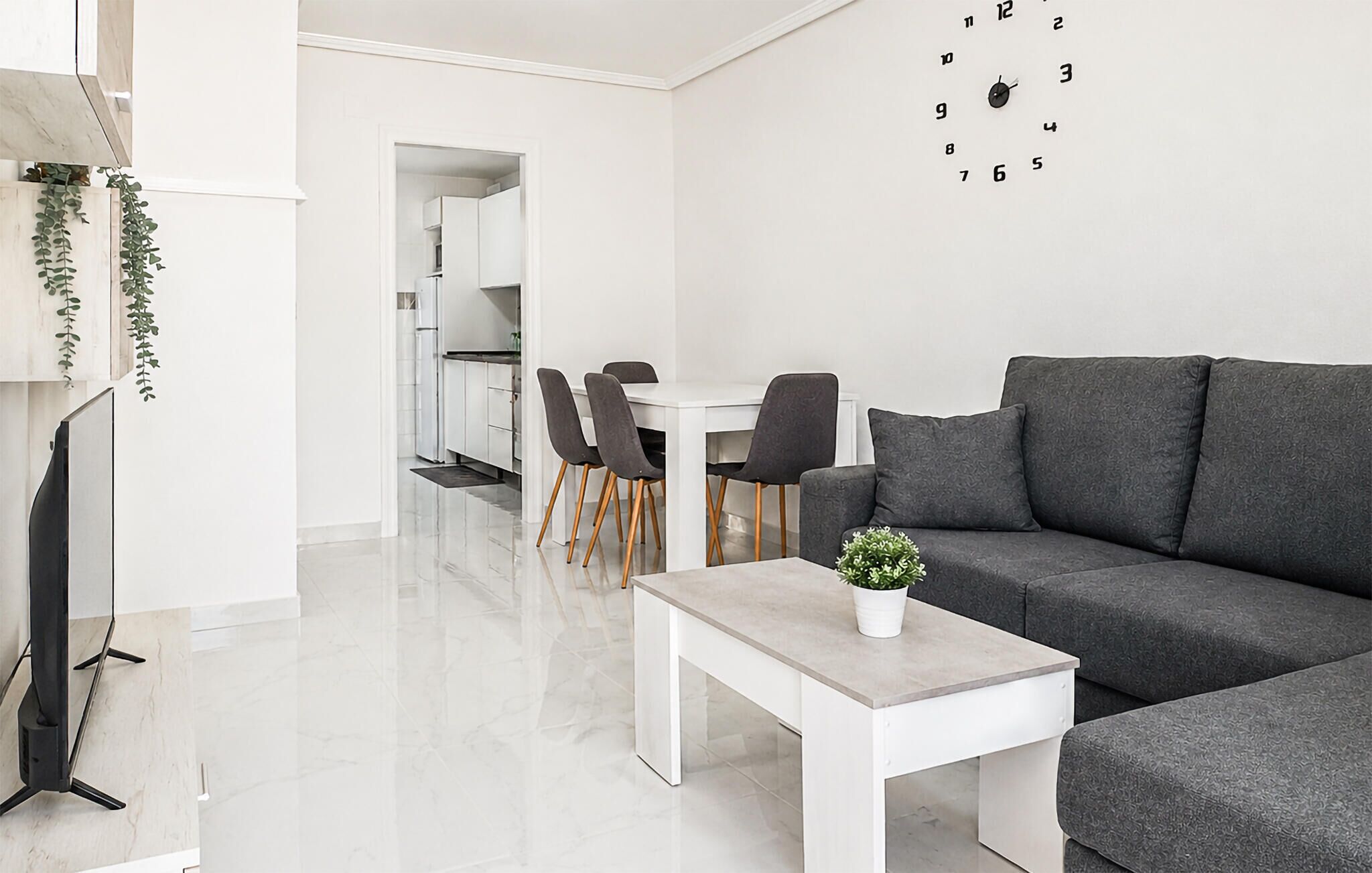 A modern living room with a grey sofa, a white coffee table, and a dining area with chairs and a table.