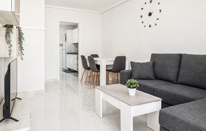 Ein modernes Wohnzimmer mit grauem Sofa, einem weißen Couchtisch und einem Essbereich mit Stühlen und Tisch.
