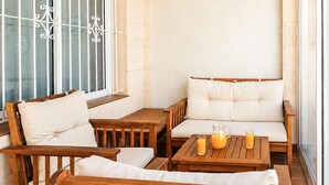 A cozy outdoor seating area with wooden furniture and cushioned benches, a glass table with drinks, and a view through a window with decorative metal bars. - Pet friendly home in Torrevieja with WiFi (Torrevieja)