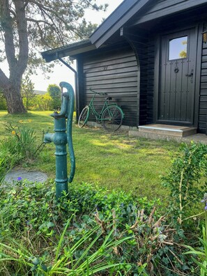 Ein Haus mit dunkler Fassade, ein Fahrrad davor abgestellt und ein grüner Feuerlöscher im Vordergrund.