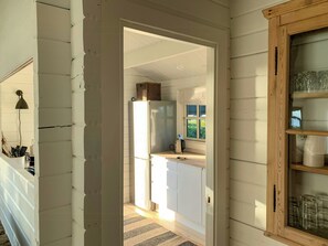 A narrow hallway leading to a kitchen with white cabinets, a refrigerator, and a window with blinds. - Panoramic view over Storebælt from Drøsselbjerg (Slagelse)