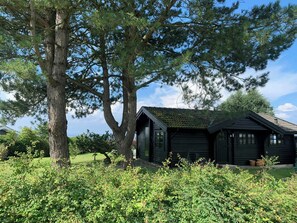 A cabin with a sloped roof, surrounded by dense greenery and a large tree. - Panoramic view over Storebælt from Drøsselbjerg (Slagelse)