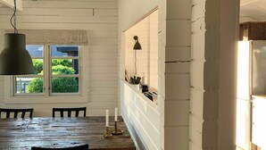 A dining area with a wooden table and chairs, a window with a view of greenery, and a hanging light fixture. - Panoramic view over Storebælt from Drøsselbjerg (Slagelse)