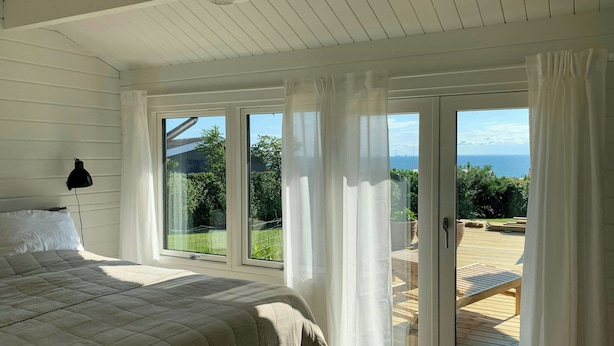 A bedroom with a large bed, a window, and a view of a wooden deck. - Panoramic view over Storebælt from Drøsselbjerg (Slagelse)