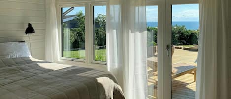 A bedroom with a large bed, a window, and a view of a wooden deck.