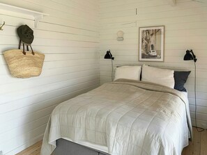 Ein Schlafzimmer mit einem Bett, zwei Nachttischlampen, einem Wandkorb und einem gerahmten Bild.