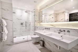 Een moderne badkamer met een douche met glazen wand, een dubbele wastafel en een grote spiegel.