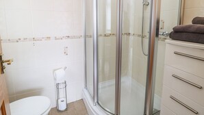 Ein Badezimmer mit einer Duschkabine, einer Toilette und einem Waschtisch mit Schubladen.