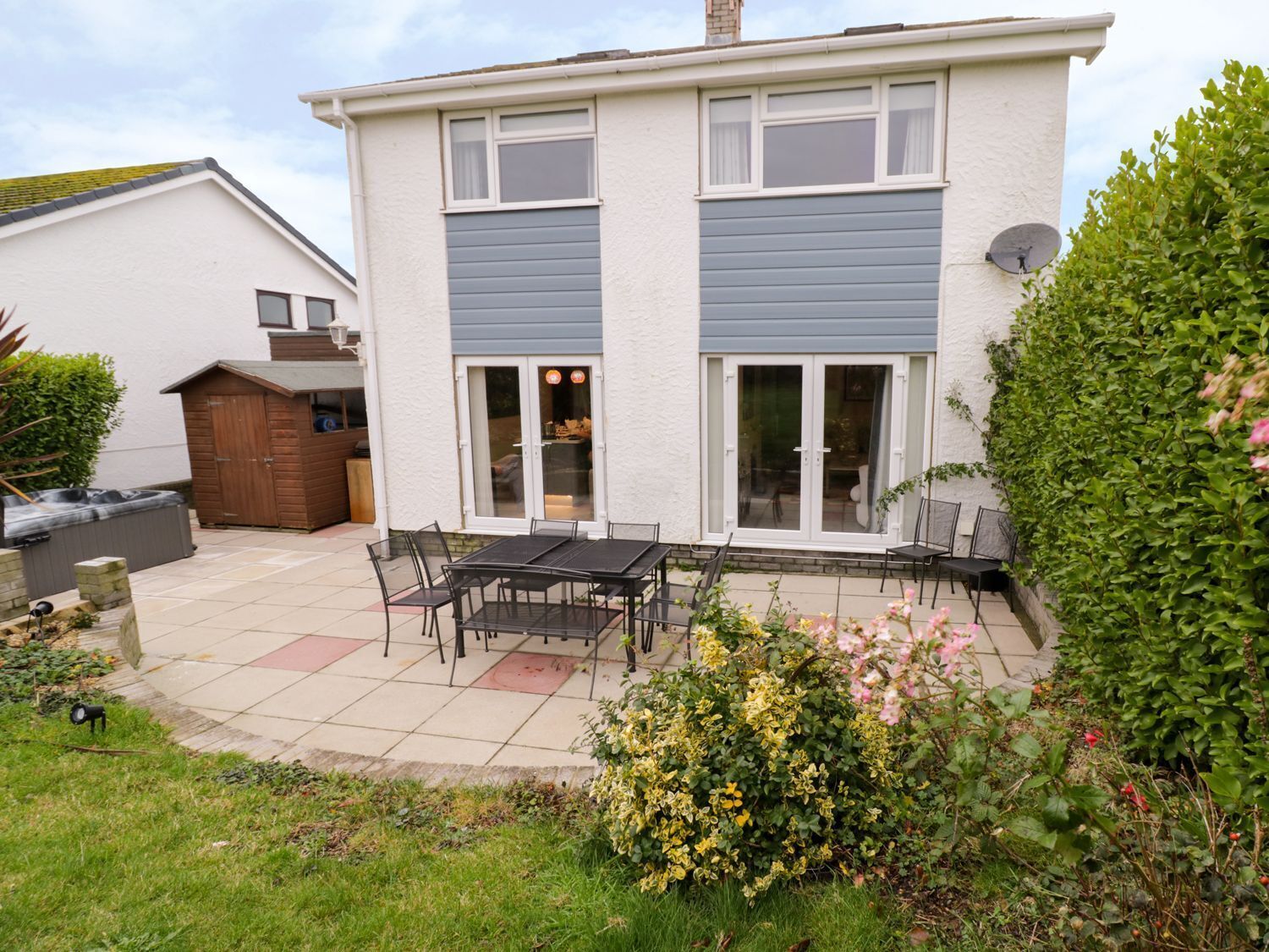 Een twee verdiepingen tellend huis met een patio voorzien van een tafel, stoelen, een jacuzzi en een tuinhuis.