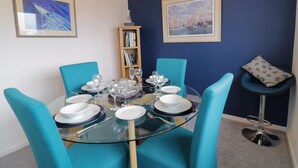 Un comedor con una mesa de vidrio rodeada de sillas color turquesa, una estantería y obras de arte enmarcadas en las paredes.