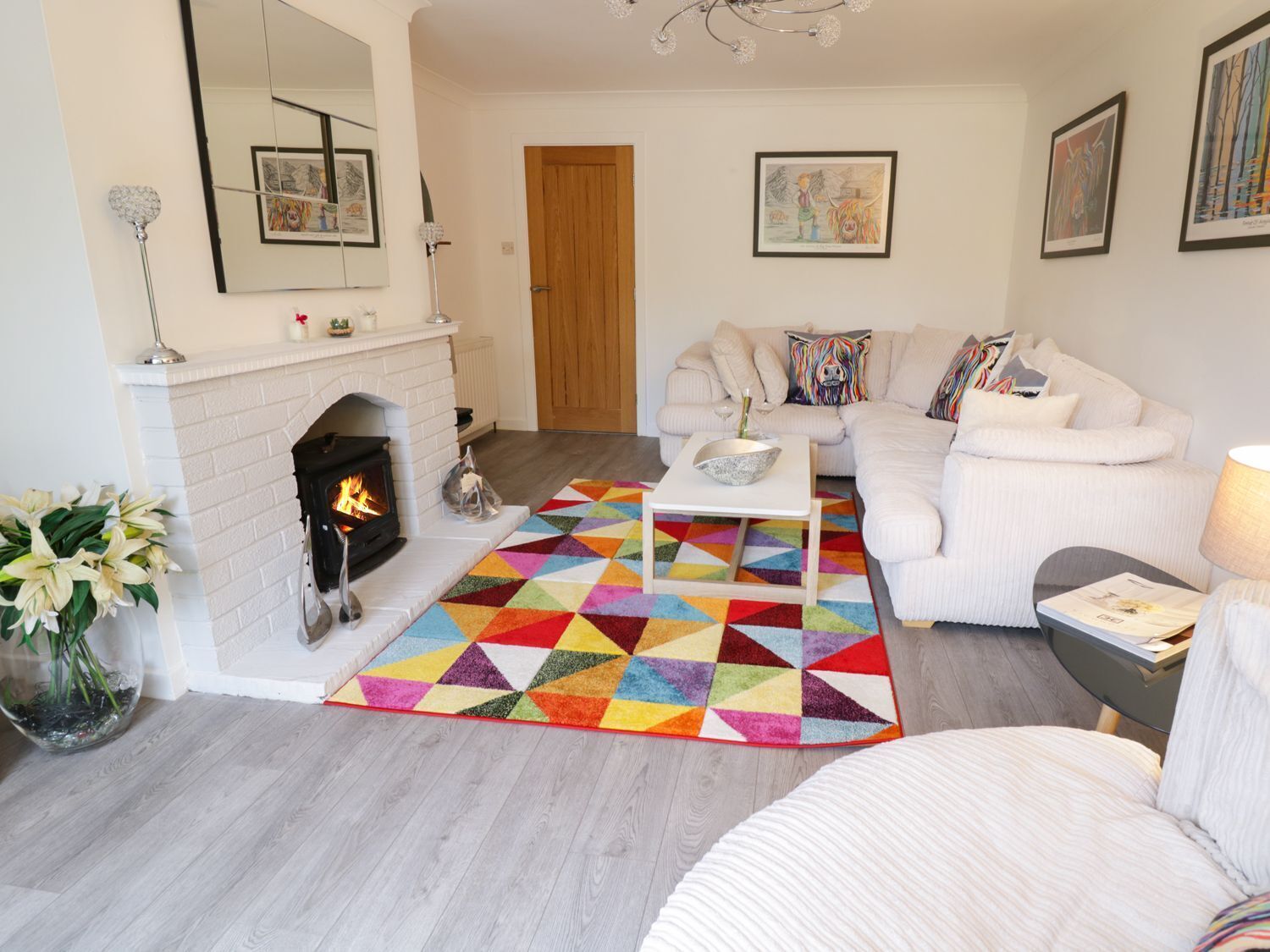 A living room with a fireplace, a white sofa set, a colorful geometric rug, and artwork on the walls.