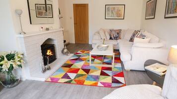 A living room with a fireplace, a white sofa set, a colorful geometric rug, and artwork on the walls.