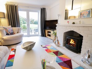 A living room with a fireplace, a sofa, a television, and a large window. - Gwelfor (Cemaes Bay)