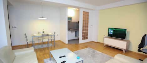 A modern living room with a sofa, a coffee table, a TV, and a dining area with chairs and a table.