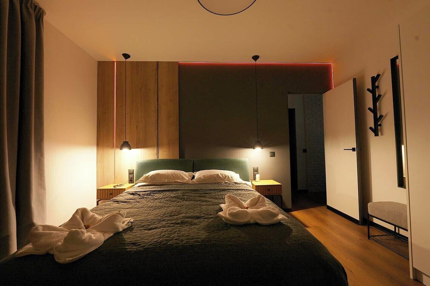 Une chambre d’hôtel comprenant un lit, des lampes de chevet, une armoire en bois, une table de chevet et une porte avec un porte-manteau.