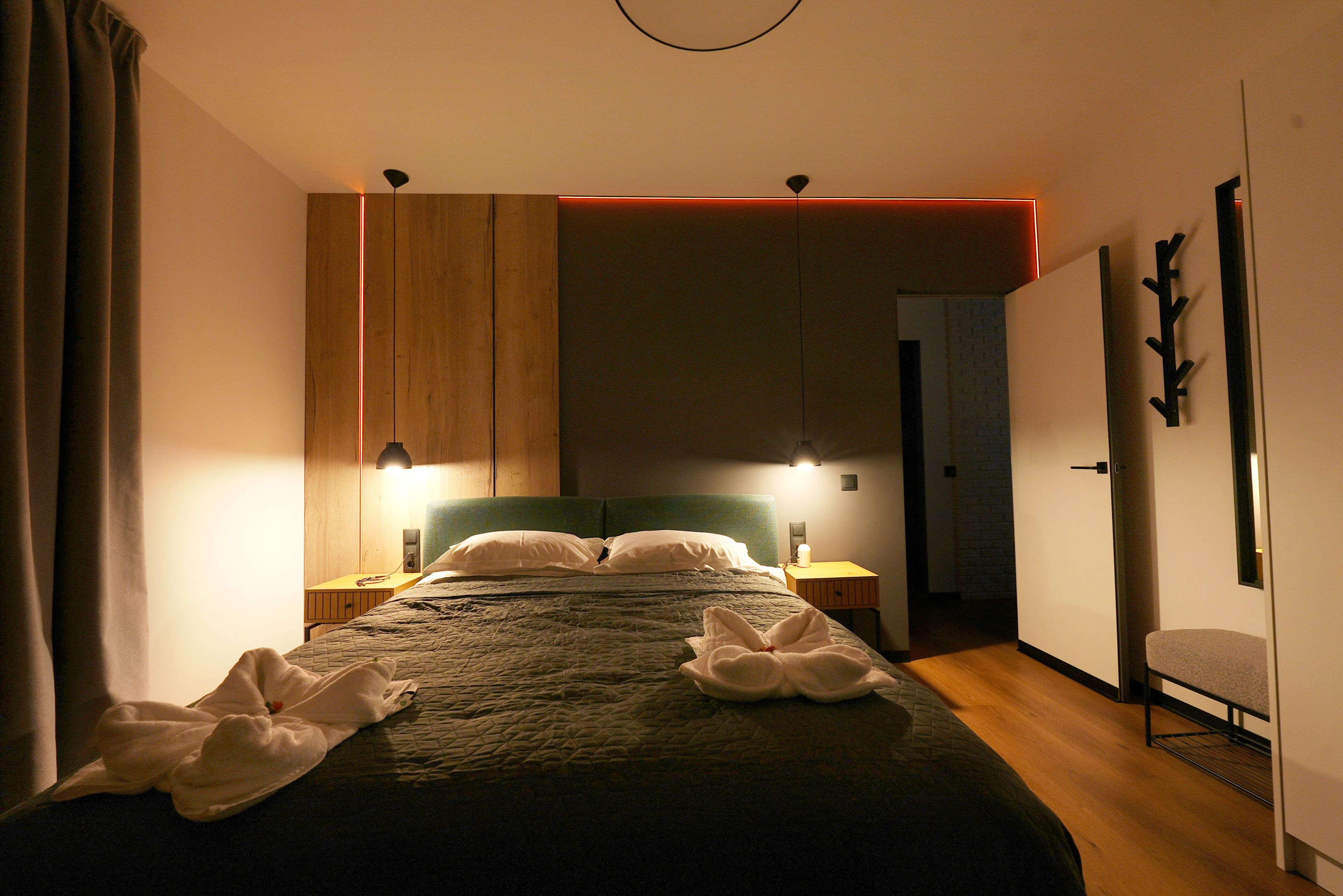 Una camera d'albergo moderna con un letto grande, lampade sui comodini, un armadio in legno e vista sul corridoio.