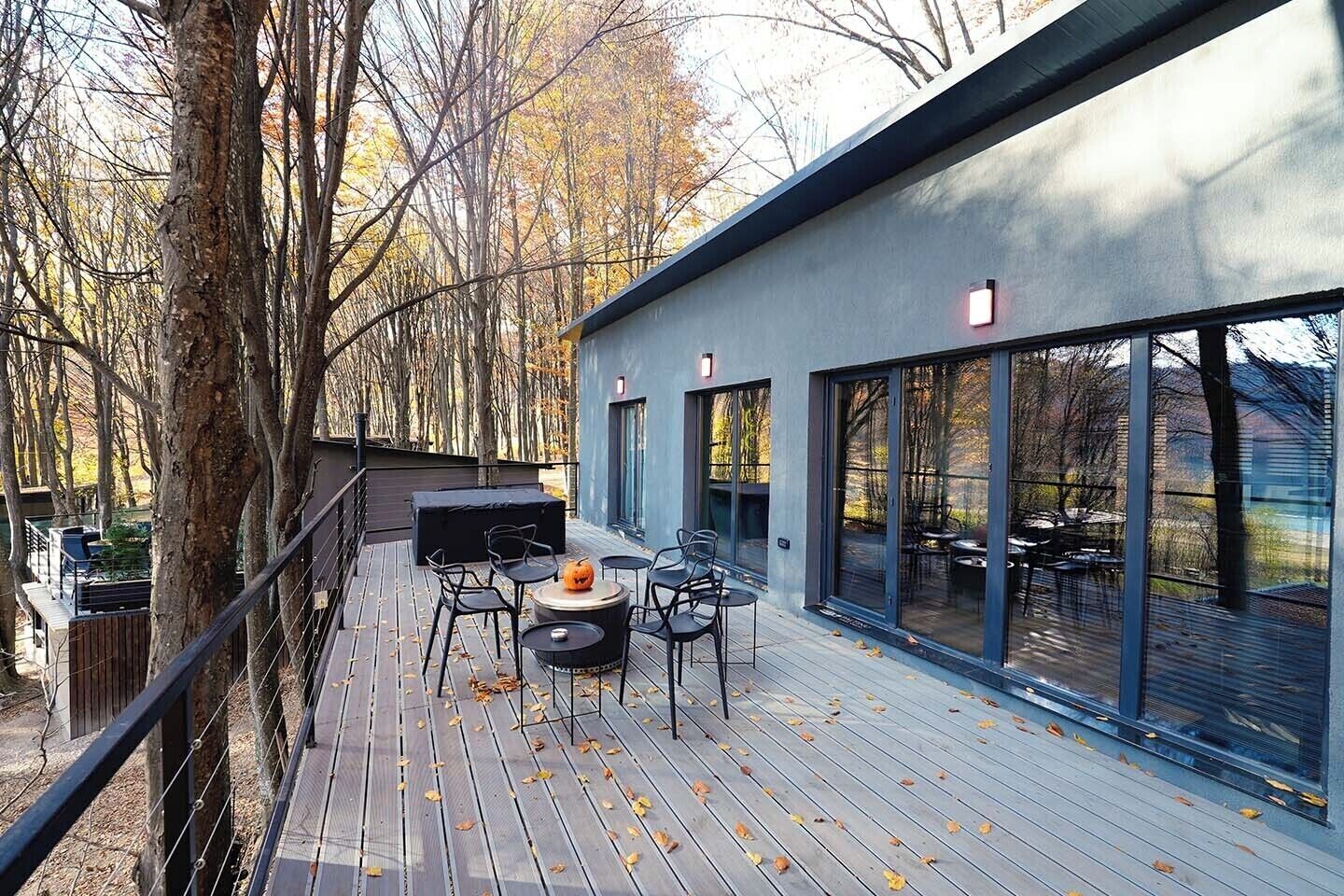 Een modern terras buiten met een barbecuehoek, zitplaatsen en grote ramen.