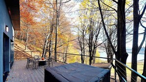 Una terraza con mobiliario exterior, un espacio de estar techado y vistas a árboles y una masa de agua.