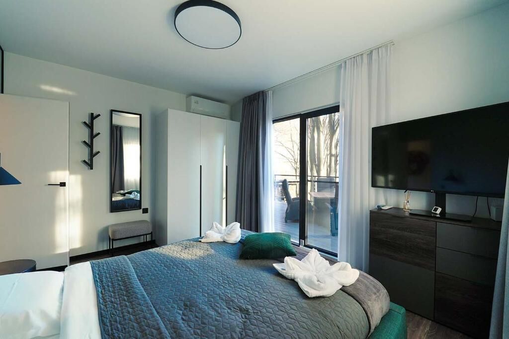 Une chambre d’hôtel moderne dotée d’un grand lit, d’un téléviseur à écran plat et d’une porte-fenêtre coulissante donnant sur l’extérieur.