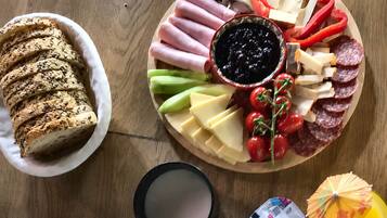 A wooden table with a variety of food items including sliced bread, cheese, meats, and a bowl of jam.