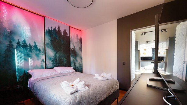Habitación de hotel moderna con una cama, un escritorio y un baño visible a través de una puerta abierta.