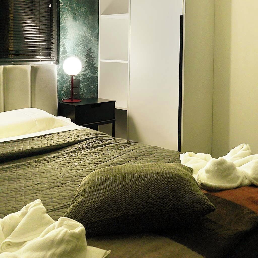 Habitación de hotel con cama, mesita de noche, lámpara y armario.