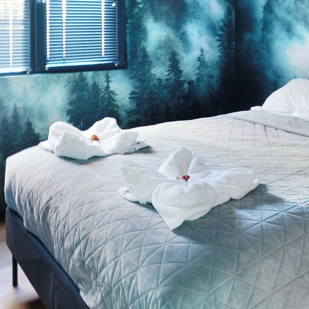 Una cama con una colcha acolchada y dos toallas blancas con forma de cisnes adornadas con flores rojas.