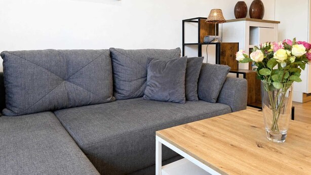 En moderne stue med en grå modulsofa, et træsofabord og en vase med blomster.