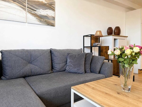 A modern living room with a grey sectional sofa, a wooden coffee table, and a vase with flowers.
