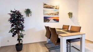 Et spiseområde med et træbord og brune stole, en potteplante og tre indrammede landskabsmalerier på væggen.