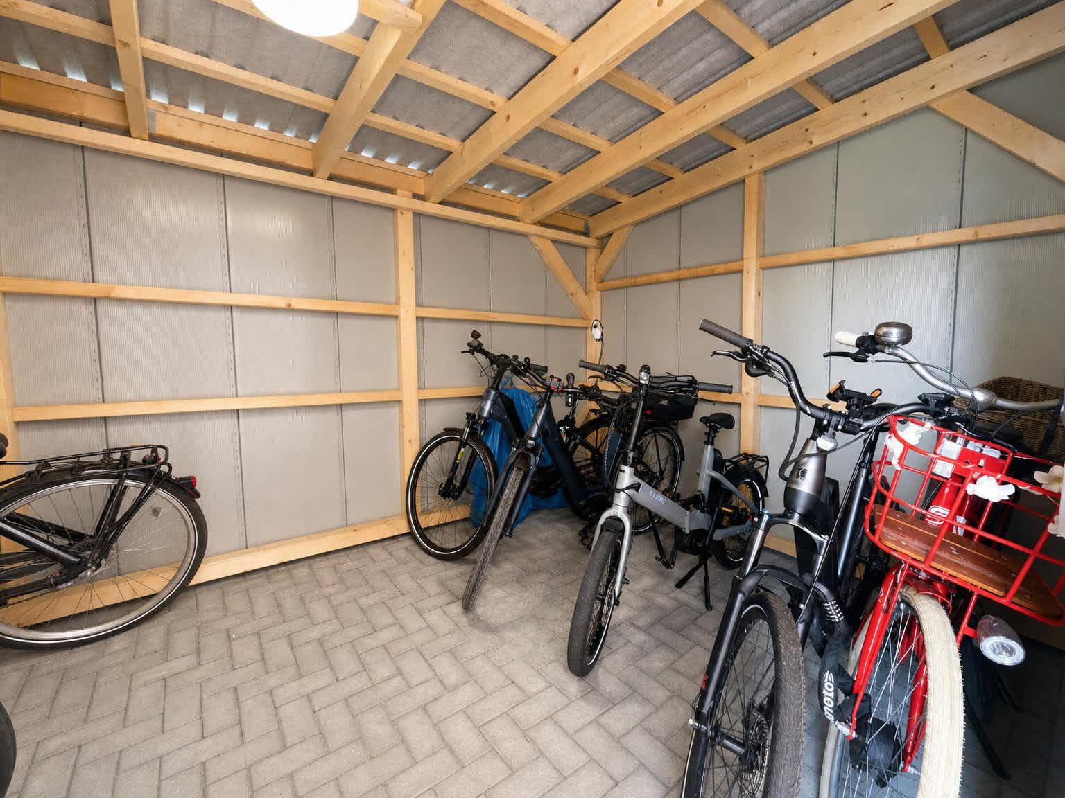 A covered bicycle storage area with multiple bicycles and a red basket.