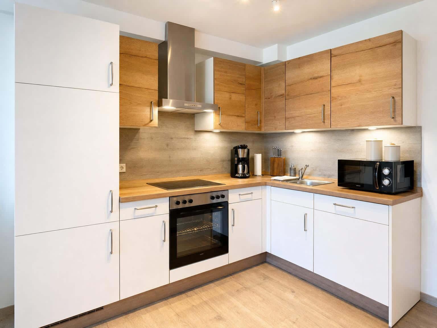 Una cocina moderna con armarios blancos, una campana extractora de acero inoxidable, horno integrado, microondas y cafetera.