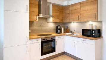 Una cocina moderna con armarios blancos, una campana extractora de acero inoxidable, horno integrado, microondas y cafetera.