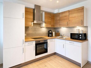 A modern kitchen with white cabinets, a stainless steel range hood, a built-in oven, a microwave, and a coffee maker. - Modern New-Build Apartment, Nottensdorf (Nottensdorf)