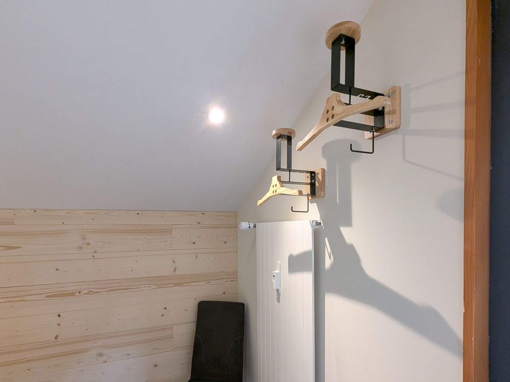 Quarto com painel de parede em madeira, uma cadeira preta e um radiador branco.