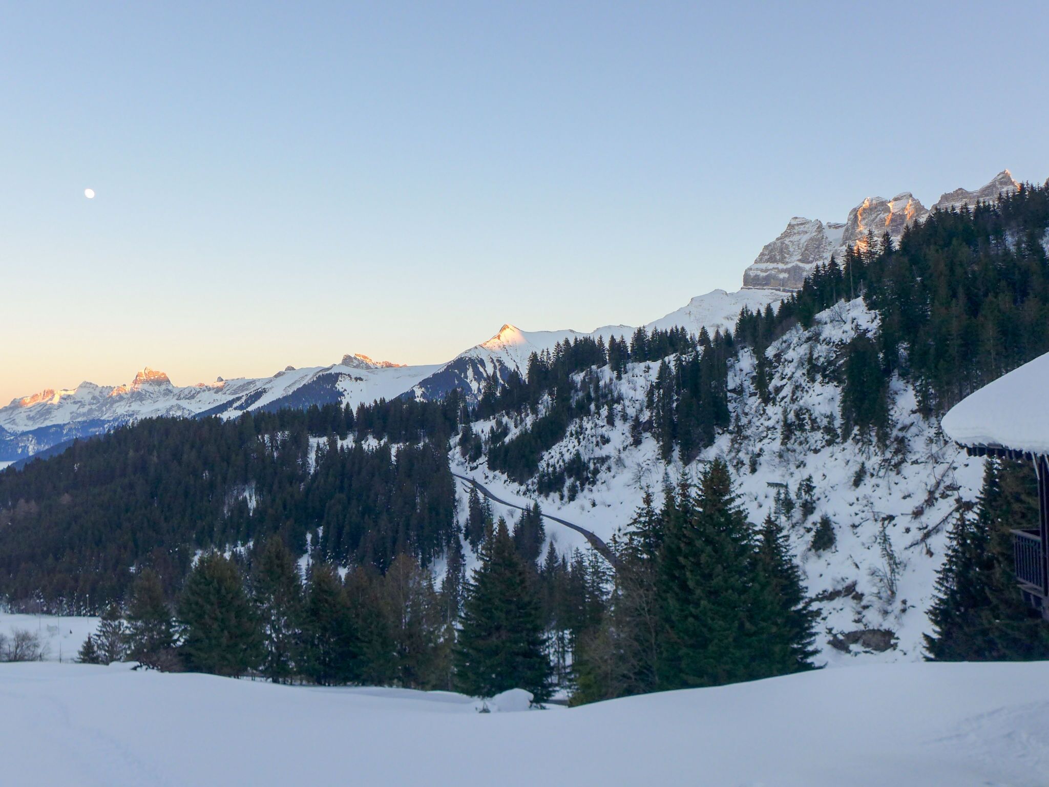 Eine verschneite Berglandschaft mit klarem Himmel und einem sichtbaren Mond.