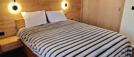 A bed with a striped blanket, wooden headboard, two bedside lamps, and a wooden wardrobe.